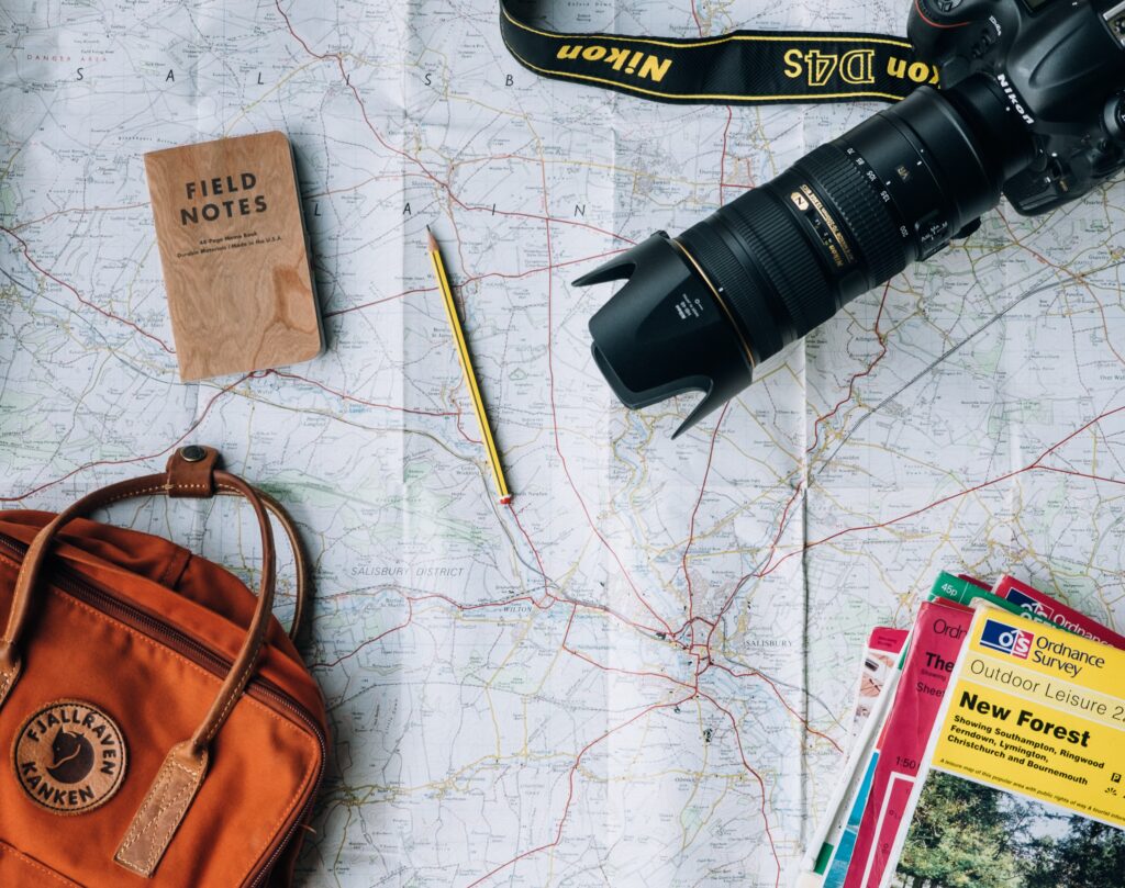 flat lay of map with camera, pencil, notebook, and travel accessories